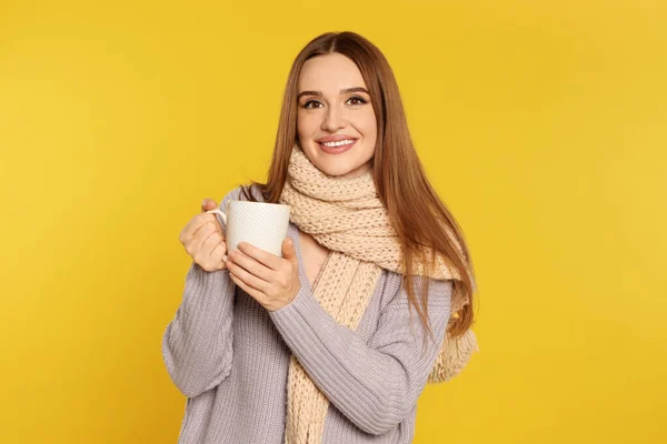 Krásná mladá žena ve svetru s pitím na žlutém pozadí. Zimní sezóna — Stock fotografie