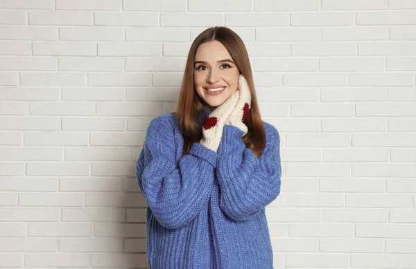 Wanita muda cantik dengan sarung tangan dan sweater biru dekat dinding bata putih. Musim dingin — Stok Foto