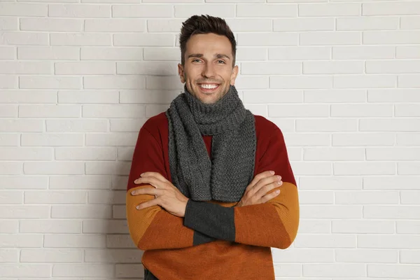 Pria muda yang bahagia dengan syal dan sweater hangat di dekat dinding bata putih. Musim dingin — Stok Foto