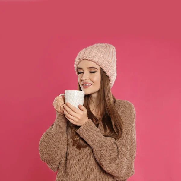 Bella giovane donna in cappello e maglione con bevanda su sfondo rosa. Stagione invernale — Foto Stock