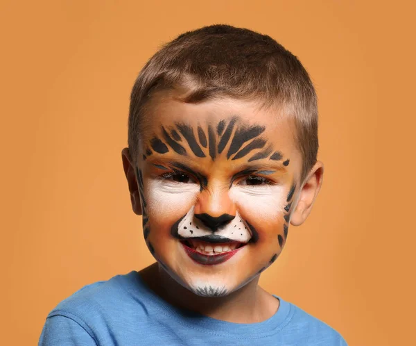 Garotinho bonito com pintura facial no fundo laranja — Fotografia de Stock