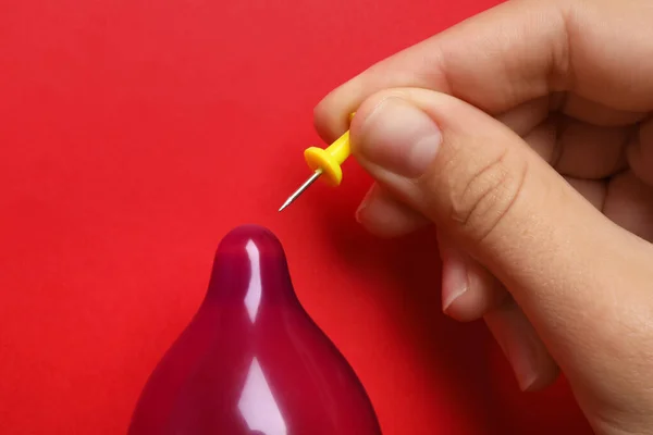 Mulher piercing preservativo inflado com pino no fundo vermelho, close-up. Sexo seguro — Fotografia de Stock