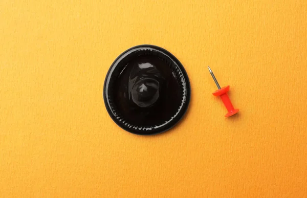 Чорний презерватив і шпилька на помаранчевому фоні, плоский — стокове фото