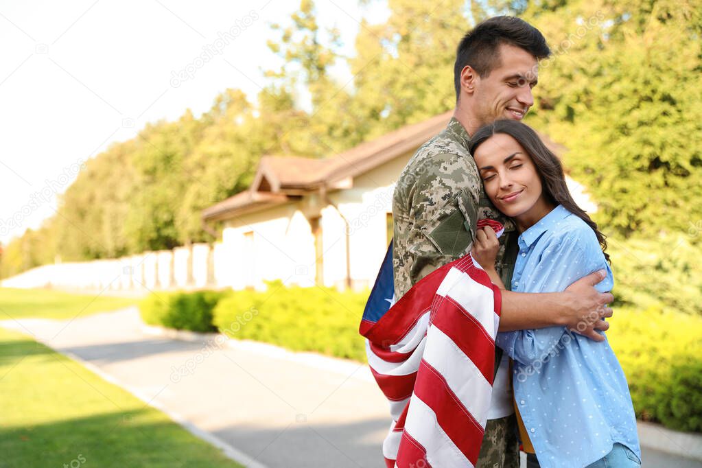 Man in military uniform with American flag hugging his wife outdoors