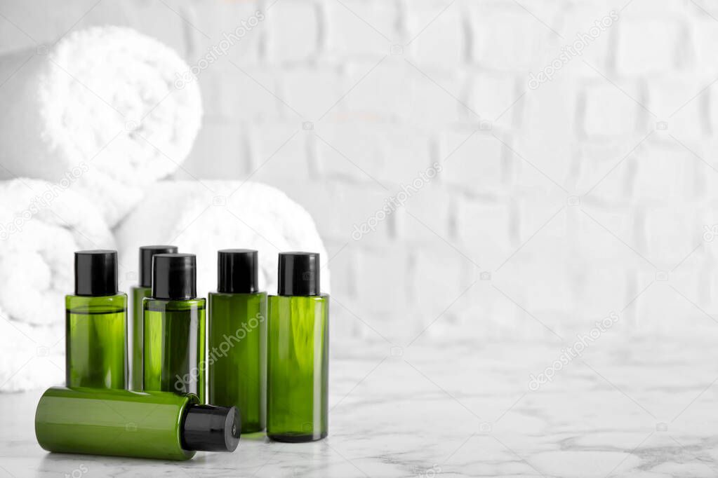 Mini bottles with cosmetic products and towels on marble table against white background. Space for text