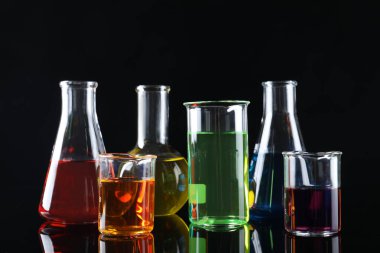Siyah zemin üzerinde renkli sıvılar bulunan laboratuvar camları.