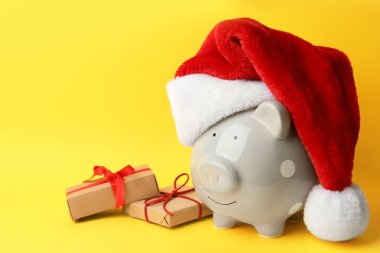 Domuz kumbarası, Noel Baba şapkası ve sarı arka planda hediye kutuları. Metin için boşluk