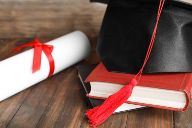 Mezuniyet şapkası, kitaplar ve öğrenci diploması ahşap masada, yakın plan.
