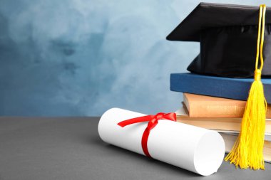 Mezuniyet şapkası, kitaplar ve öğrenci diploması açık mavi arka plana karşı gri masada. Metin için boşluk