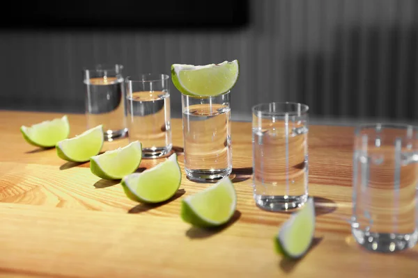 Vodka shots and lime slices on wooden bar counter — Stock Photo, Image