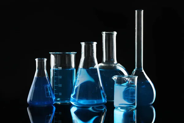 Glaswerk voor laboratoria met blauwe vloeistoffen op zwarte ondergrond — Stockfoto