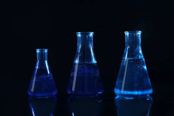Vetreria da laboratorio con liquidi su fondo nero, tonica in blu — Foto Stock