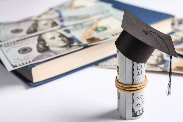 Billets en dollars avec mini chapeau de graduation étudiant et livre sur fond blanc. Concept de frais de scolarité — Photo