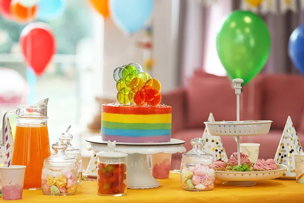 Pastel de cumpleaños brillante y otras golosinas en la mesa en la habitación decorada — Foto de Stock