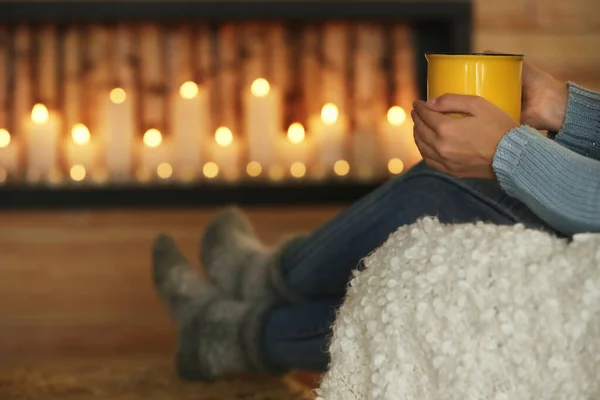 Mujer con taza de bebida caliente cerca de chimenea decorativa en el interior, primer plano. Ambiente de invierno — Foto de Stock