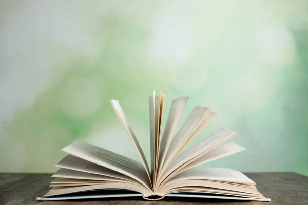 Livro aberto sobre mesa de madeira contra fundo verde desfocado — Fotografia de Stock