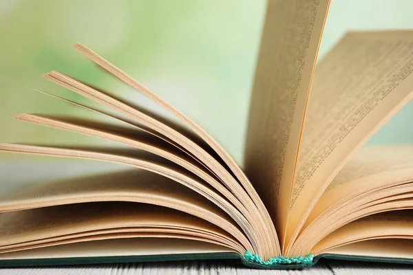 Livro aberto sobre mesa de madeira branca contra fundo verde desfocado, close-up — Fotografia de Stock