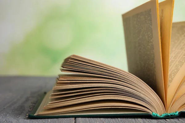 Livro aberto sobre mesa de madeira cinza contra fundo verde desfocado, close-up — Fotografia de Stock