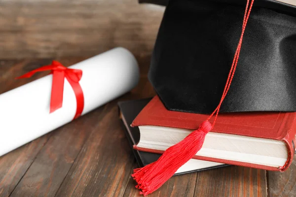 Sombrero de graduación, libros y diploma de estudiante en mesa de madera, primer plano — Foto de Stock