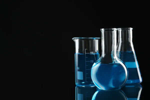 Laboratory glassware with blue liquids on black background. Space for text — Stock Photo, Image