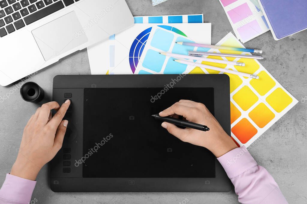Female designer working with graphic tablet at grey stone table, top view