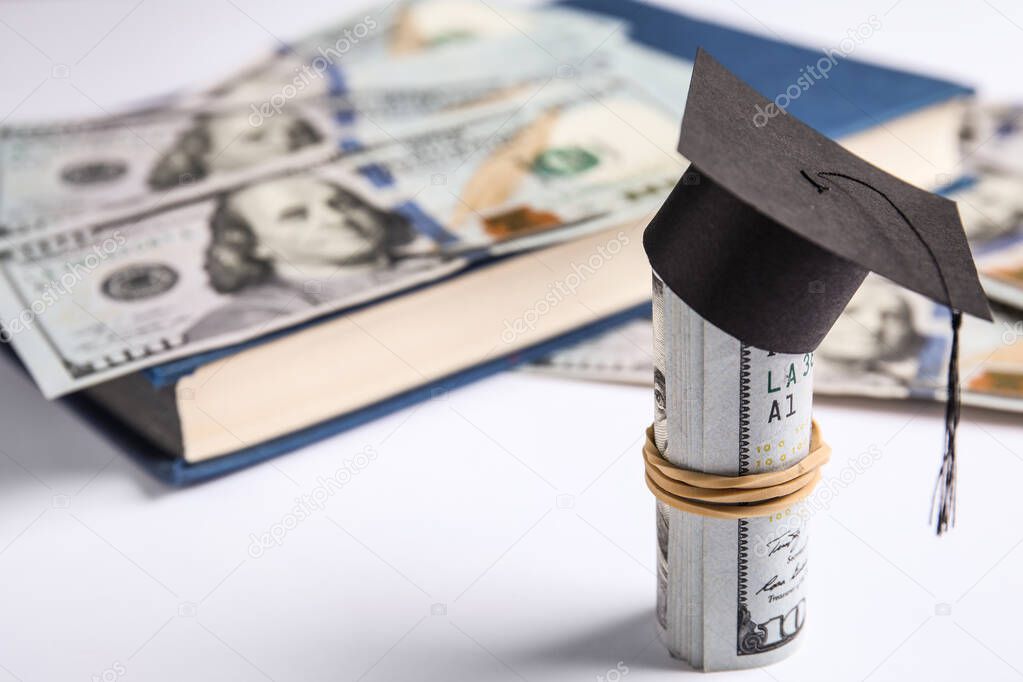 Dollar banknotes with mini student graduation hat and book on white background. Tuition fees concept