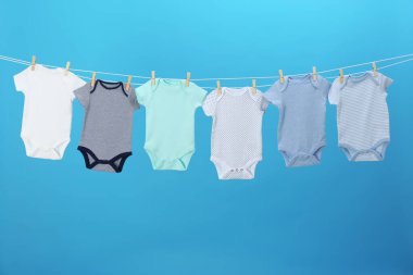 Mavi arka planda çamaşır ipinde asılı renkli bebek tulumları. Çamaşır günü