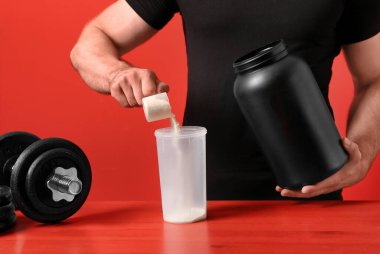 Tahta masada kırmızı arkaplana karşı protein içeceği hazırlayan adam, yakın plan.