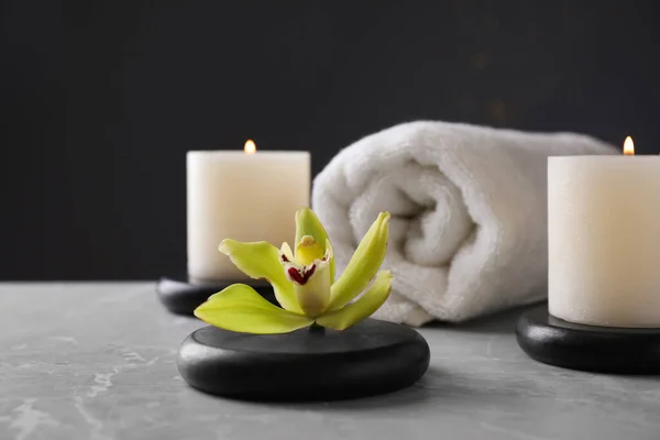Pierres de spa avec fleur exotique et bougies allumées sur table grise sur fond sombre, espace pour le texte — Photo