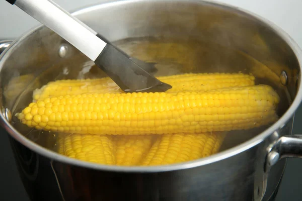 Получение свежей кукурузы из кастрюли с горячей водой на плите — стоковое фото