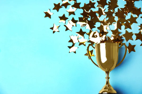 Zlatý pohár s trofejemi a konfety na světle modrém pozadí, plochý ležel. Mezera pro text — Stock fotografie