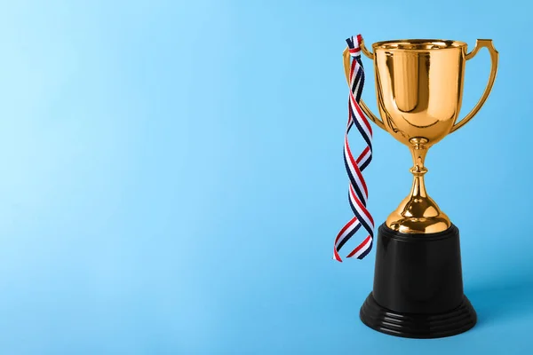 Golden trophy cup with ribbon on blue background. Space for text