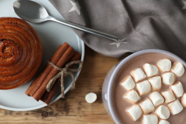 Composition with delicious hot cocoa drink and bun on wooden background, flat lay — Stock Photo, Image