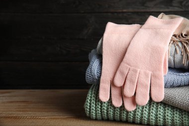 Ahşap masaya kazak ve eldivenler yığılmış. Arka planda koyu bir arka plan var. Kısa mesaj için yer var. Sonbahar giysileri
