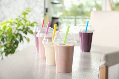 Beyaz ahşap masada plastik bardaklarda farklı milkshake 'ler.