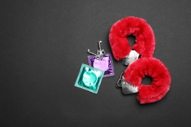 Siyah arka planda tüylü kelepçeler ve prezervatifler. Üstü açık, yazı için yer var. Seks oyunu