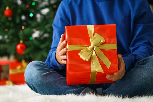 Мужчина в голубом свитере с рождественским подарком сидит дома на пушистом ковре, крупным планом — стоковое фото