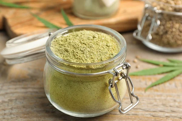 Jar of hemp protein powder on wooden table, closeup