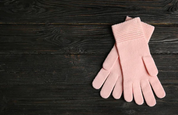 Stylish pink gloves on dark wooden background, top view with space for text. Autumn clothes