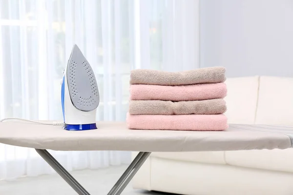 Nowe nowoczesne żelazo i czyste ręczniki na pokładzie w pomieszczeniu. Dzień prania — Zdjęcie stockowe