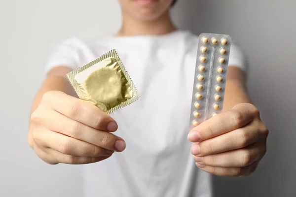 年轻妇女在浅灰背景下持有避孕药和避孕套，特写镜头。 安全性行为概念 — 图库照片