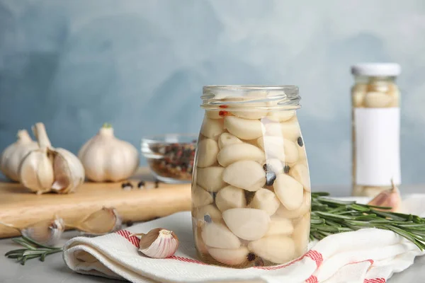 Composition with jar of pickled garlic on grey table against blue background — Stock Photo, Image