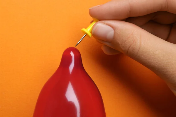 Mulher piercing preservativo inflado com pino no fundo laranja, close-up. Sexo seguro — Fotografia de Stock