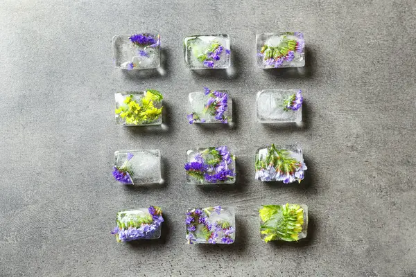 Cubos de hielo con flores sobre fondo de piedra gris, plano — Foto de Stock