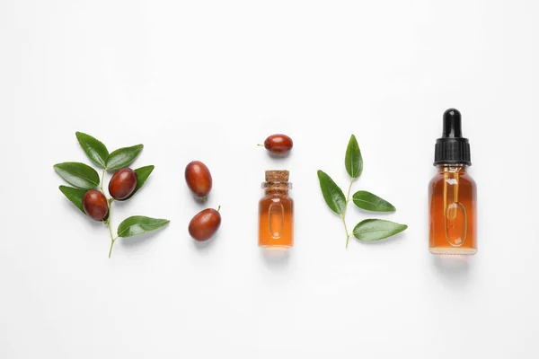 Glass bottles with jojoba oil and seeds on white background, top view — Stock Photo, Image