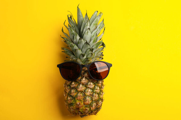 Pineapple with stylish sunglasses on yellow background, top view