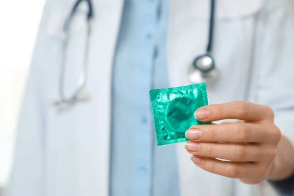 Ženský doktor držící kondom, detailní záběr. Bezpečný sexuální koncept — Stock fotografie