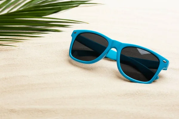 Óculos de sol elegantes e folha tropical na areia branca, espaço para texto. Tempo de férias — Fotografia de Stock