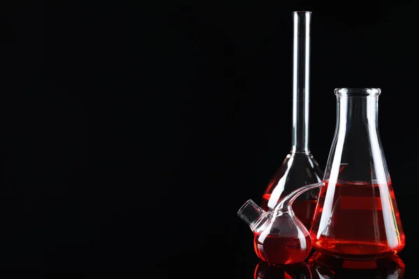 Vidros de laboratório com líquidos coloridos sobre fundo preto. Espaço para texto — Fotografia de Stock