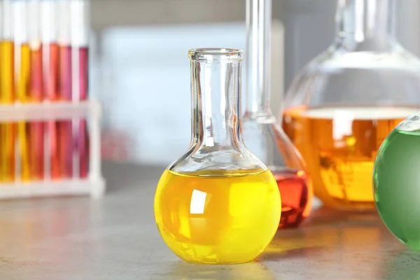 Florens kolv med färgrik vätska på gråstensbord i laboratorium — Stockfoto